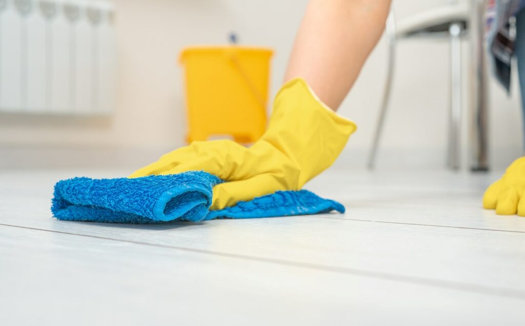 A gloved hand wipes down the inside of a fridge with a microfiber cloth