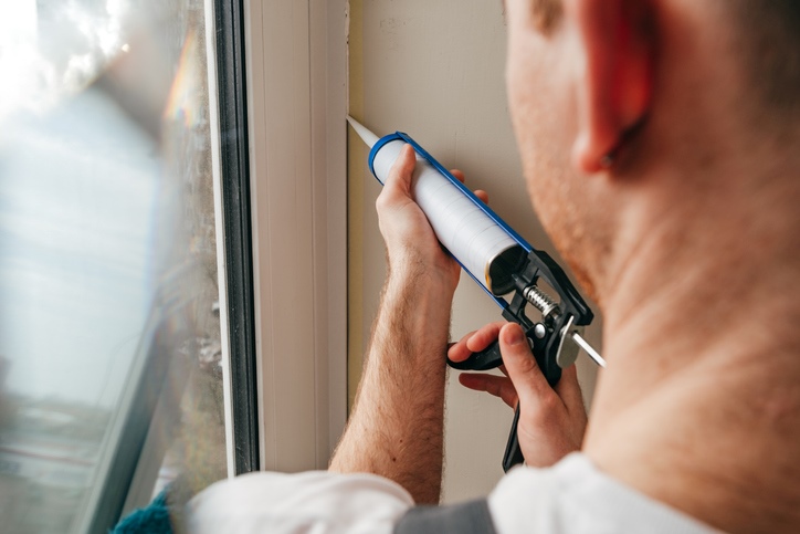 A man uses a caulk gun to seal a crack around his window