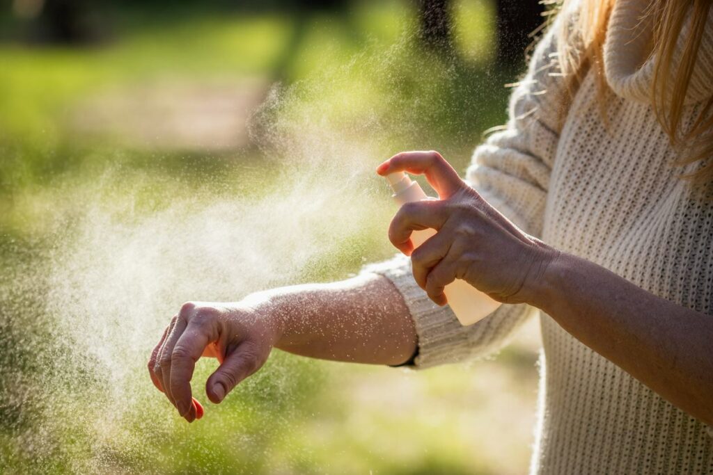 A person applying bug spray on their arm outdoors.